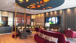 Un vestíbulo de hotel moderno con un sofá rojo, sillones grises, una recepción y un panel floral grande.