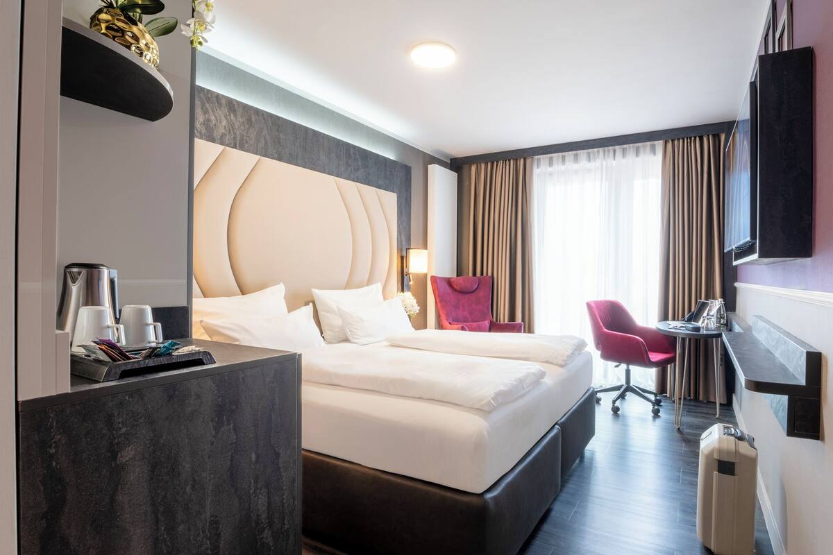 A hotel room with a bed, a desk, a chair, a TV, and a suitcase.