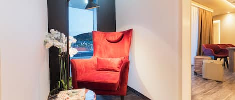 Una silla roja, una mesita con un libro y un florero con flores en una habitación de hotel.