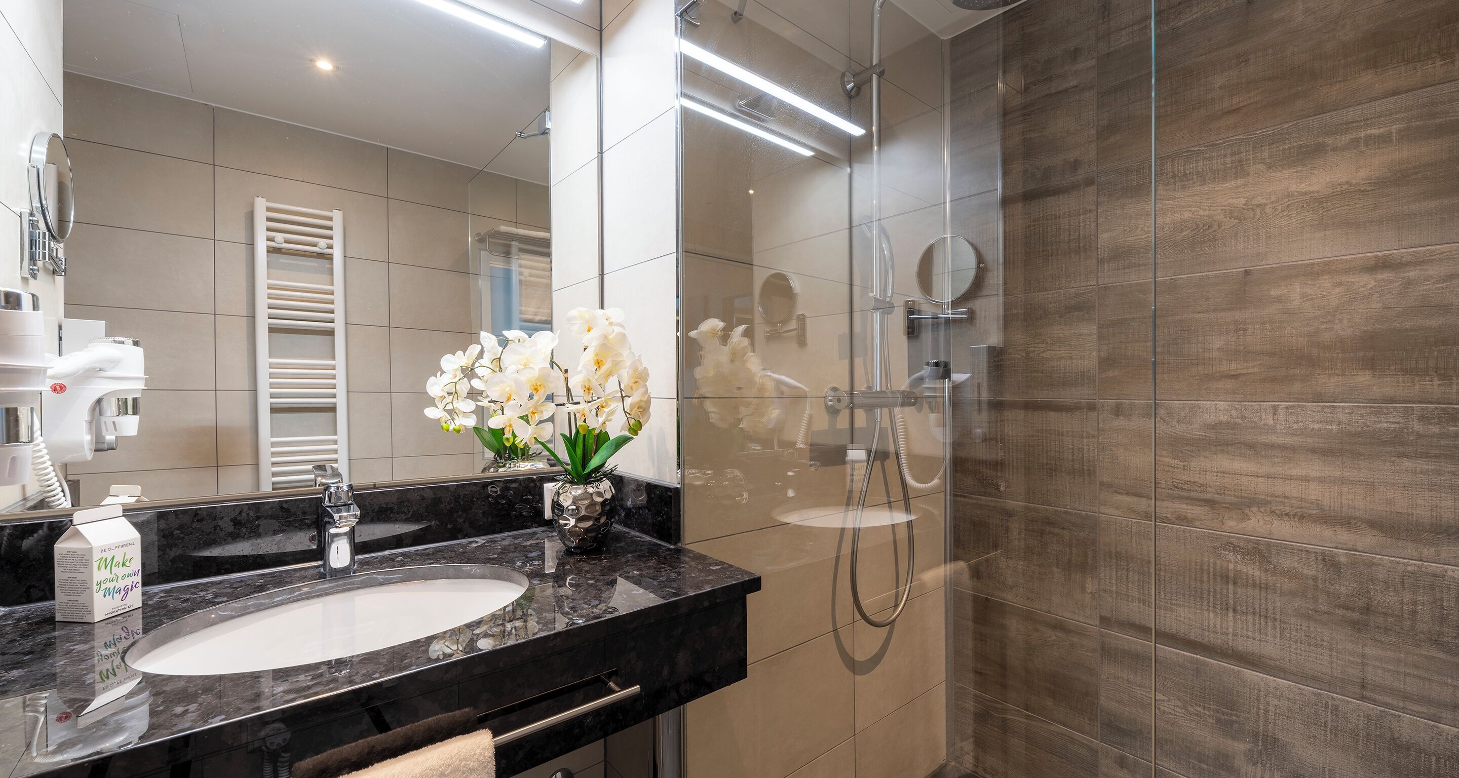 A modern bathroom with a black marble sink, a glass shower enclosure, and a towel rack.