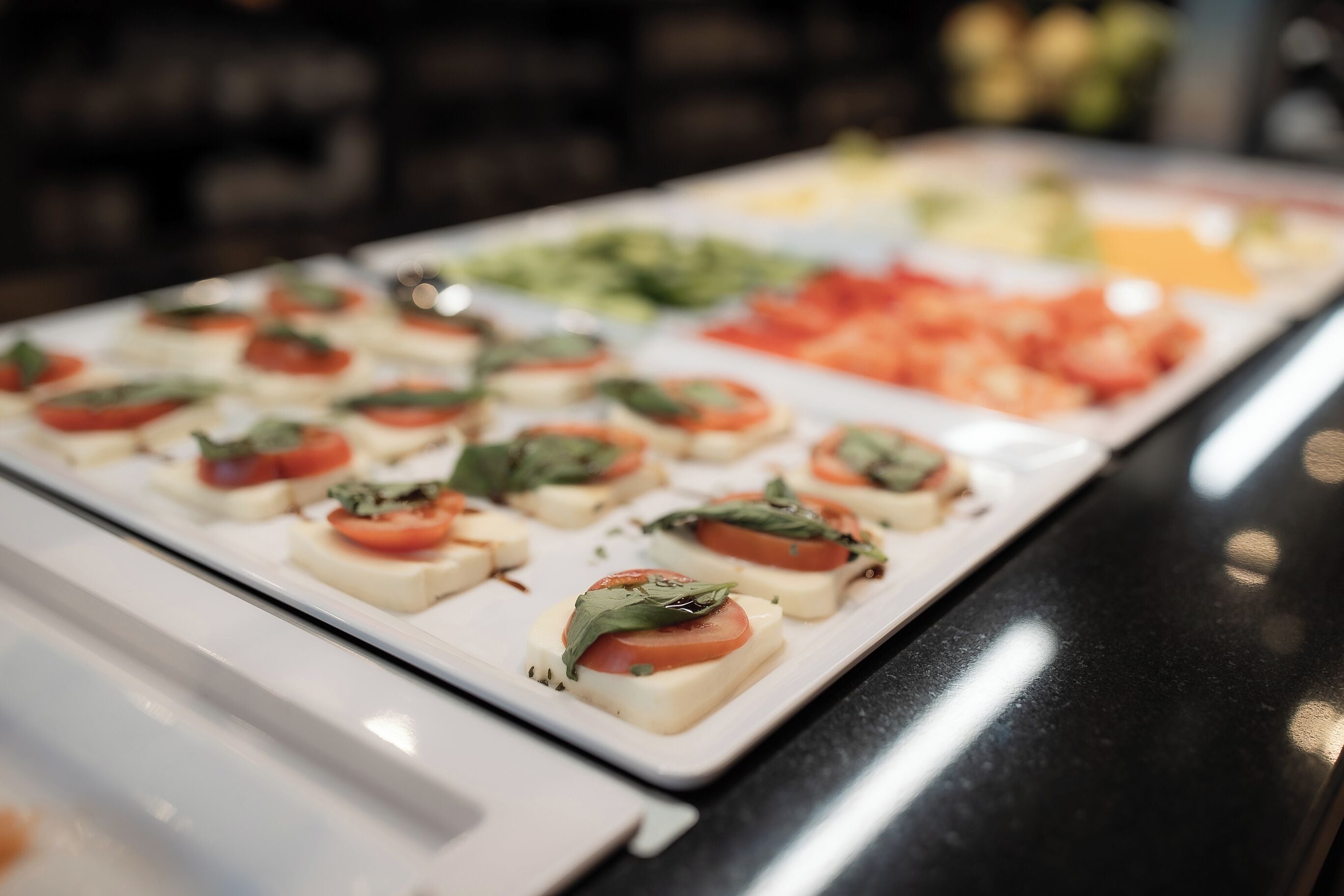 A buffet with various food options including a section with small appetizers featuring tomatoes and cheese.