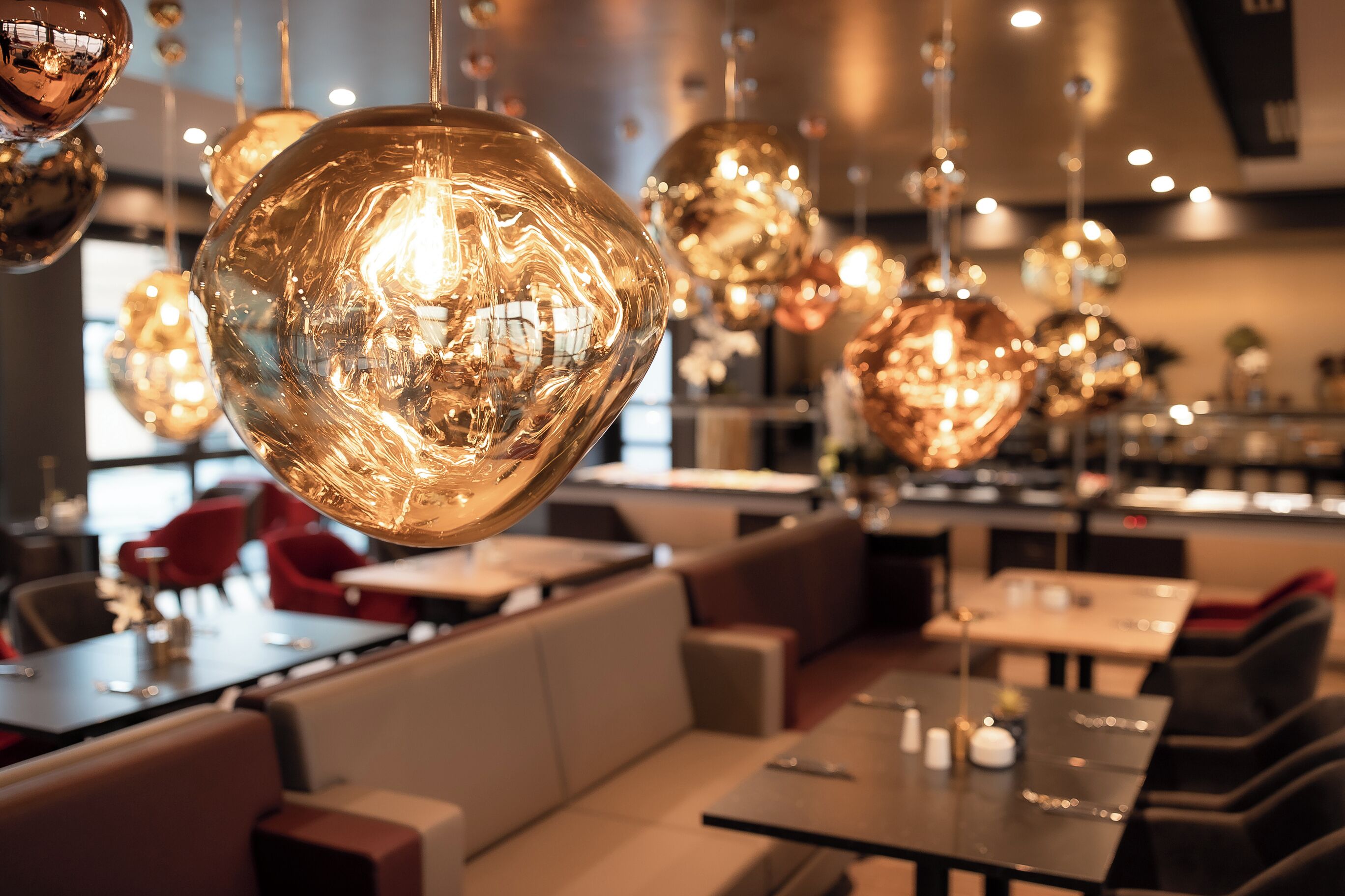 A restaurant interior with round, reflective hanging lights, cushioned seating, and a modern design.