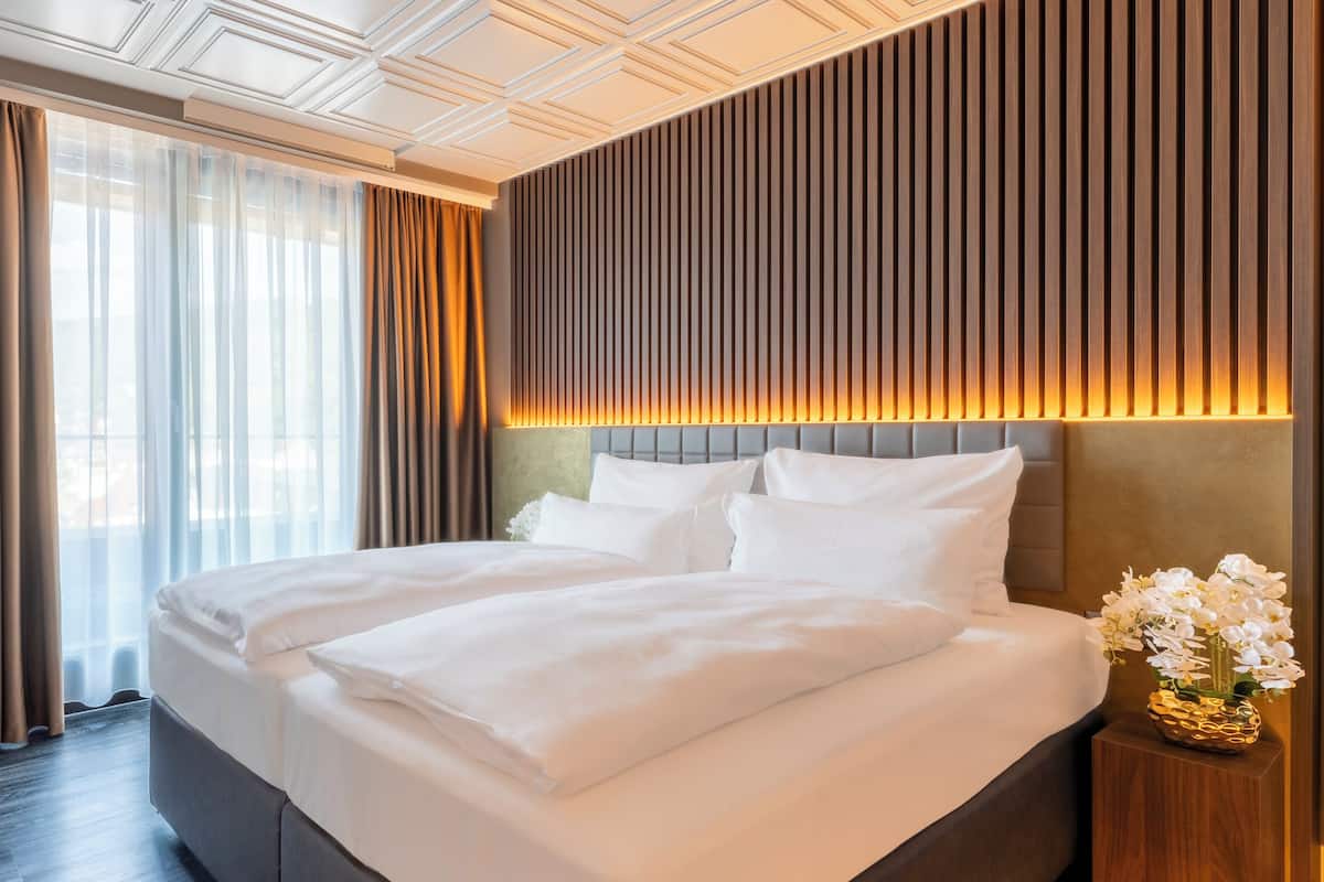 A hotel room with a large bed, a flat-screen TV, a wooden nightstand, and a vase of flowers.