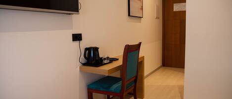 Habitación de hotel con una cama, un escritorio con una silla, un televisor montado en la pared y una puerta al fondo.