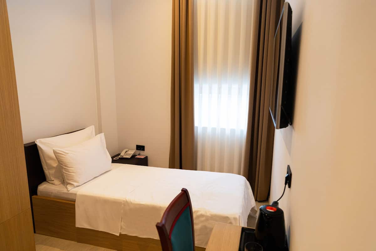 A hotel room with a bed, bedside table, chair, and a TV mounted on the wall.