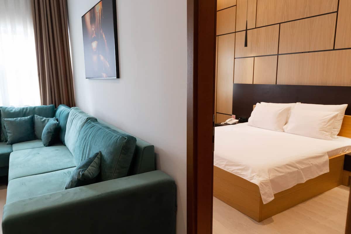 A modern hotel room with a green sofa, a wooden bed frame, and a large painting on the wall.