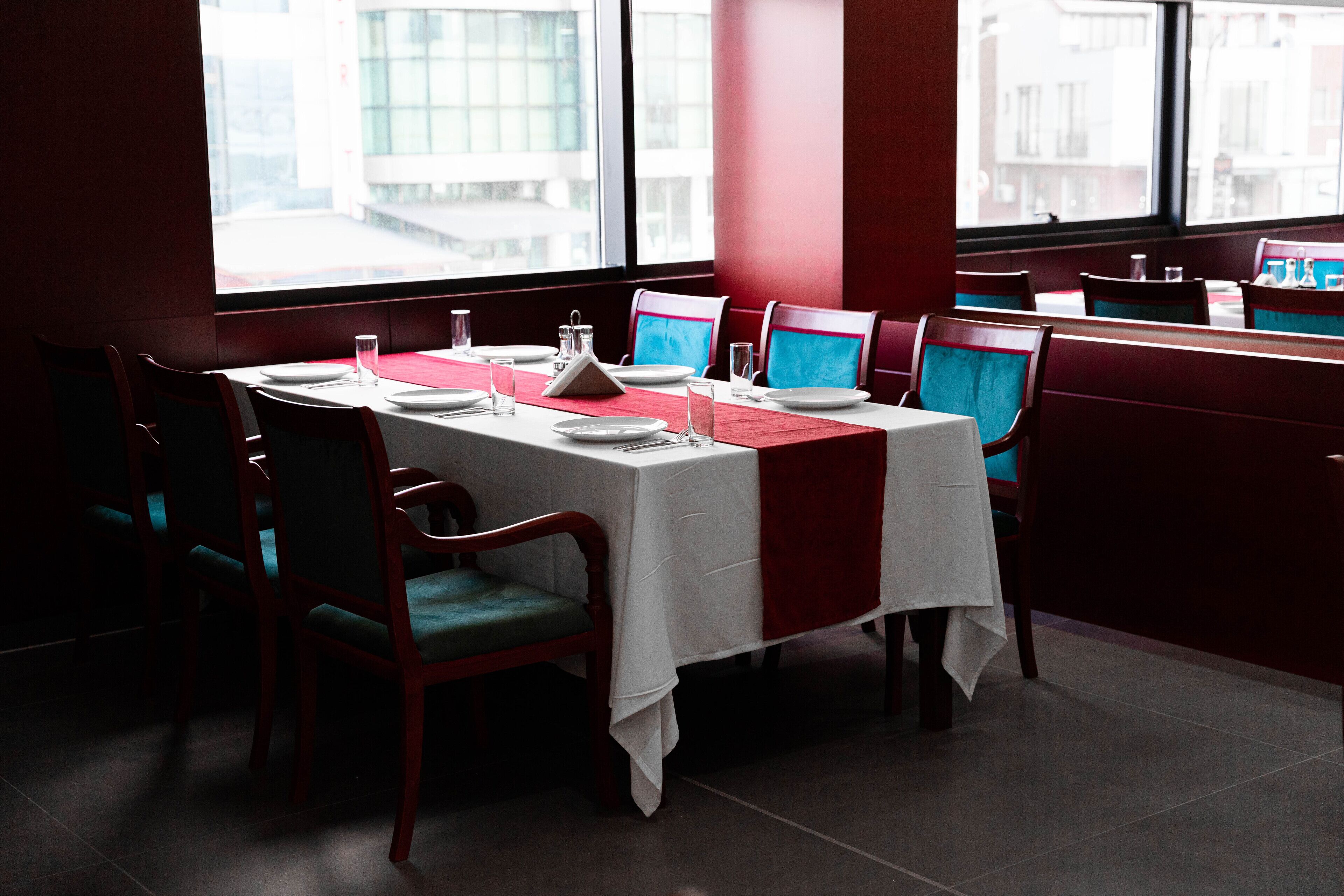 A restaurant with a table set for four, red chairs, and a view of buildings through large windows.