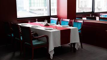 A restaurant with a table set for four, red chairs, and a view of buildings through large windows.