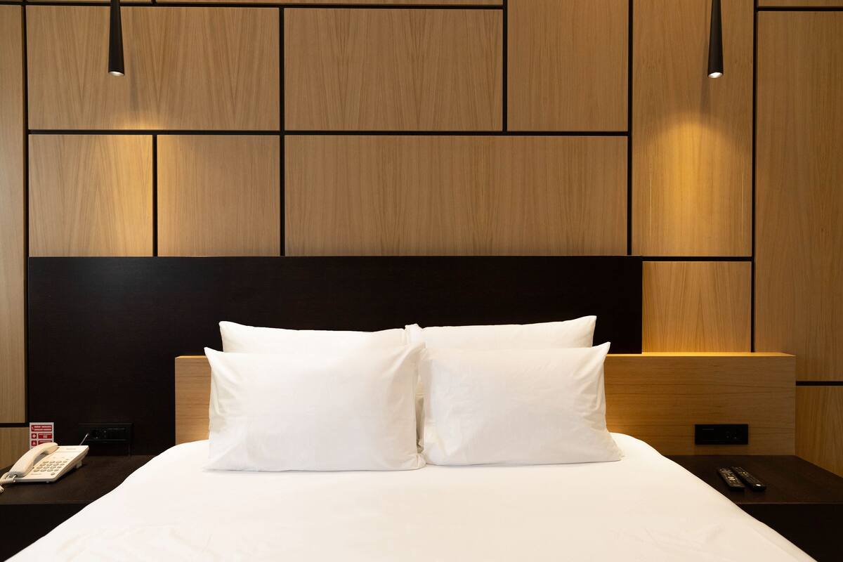 A hotel room with a large bed, two white pillows, a bedside table with a phone, and a nightstand with a remote control.