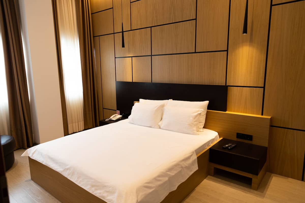 A hotel room with a large bed, a nightstand, a phone, and a wall with wooden paneling.
