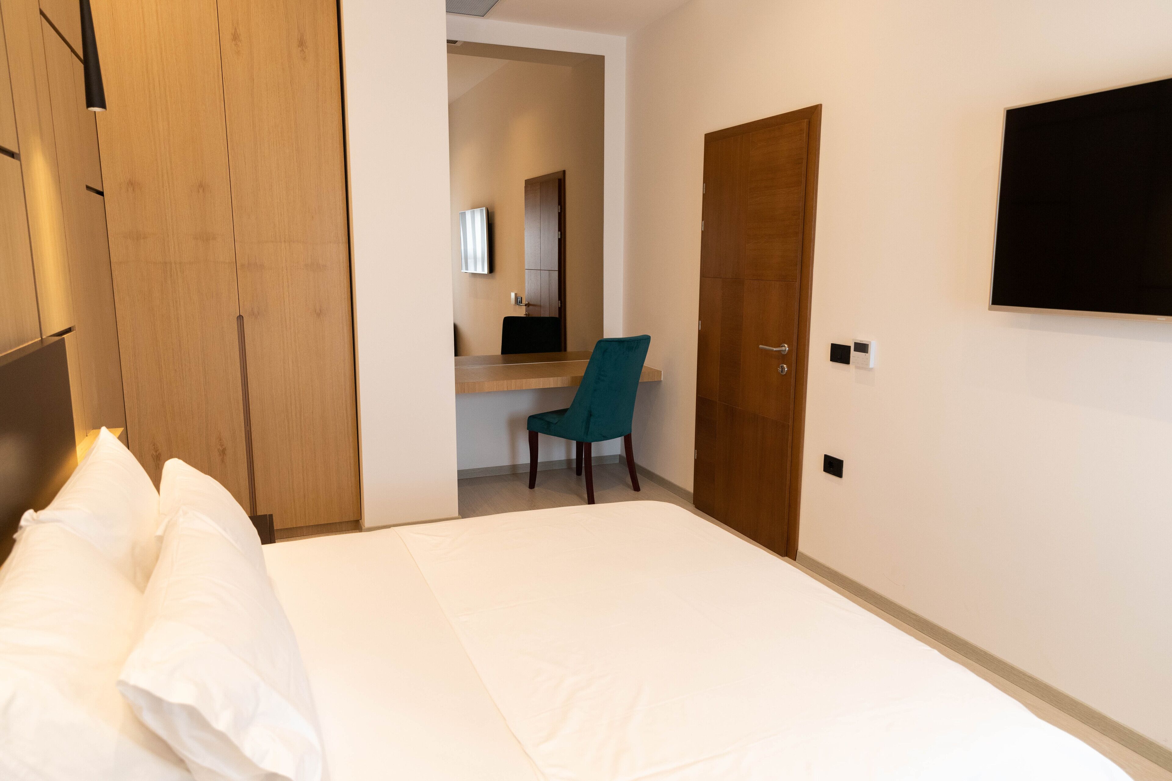 Una habitación de hotel con cama, escritorio, silla, televisor y armario.