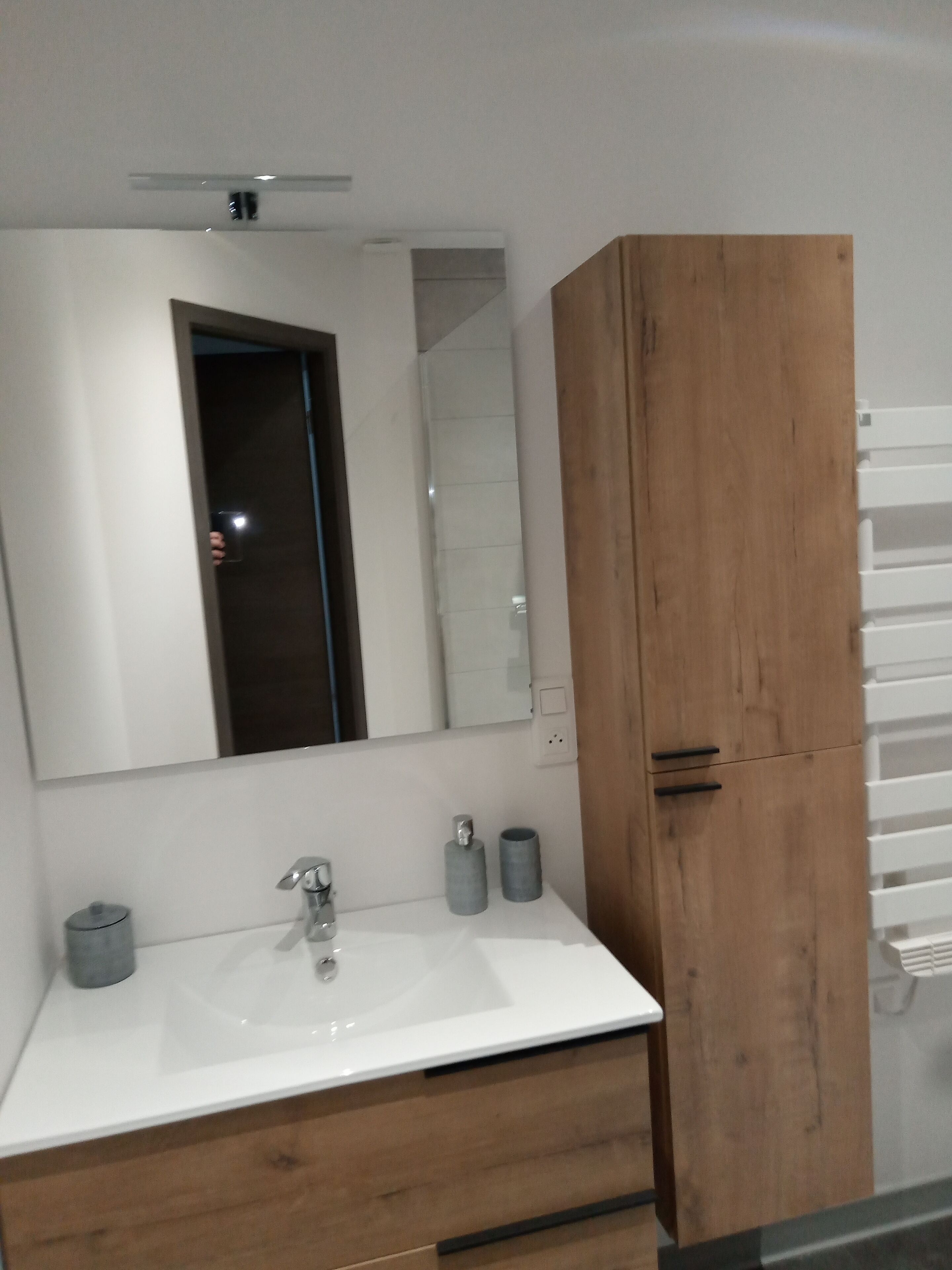A modern bathroom with a white sink, wooden cabinet, and a mirror above the sink.