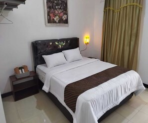 A neatly made bed with white bedding and a patterned throw, a nightstand with a basket of toiletries, a wall-mounted light, and a painting of flowers above the bed. - Borobudur Cluster Homestay Candirejo Syariah (Borobudur)