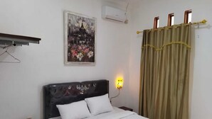 Une chambre à coucher bien rangée, avec un lit, une table de chevet, un climatiseur fixé au mur, un tableau et un rideau.