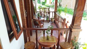 Un espace extérieur aménagé avec des meubles en bois, comprenant une table et des chaises, entouré de plantes en pot et d’un mur en briques.