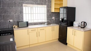 Una cocina con microondas, estufa, lavaplatos, refrigerador y una ventana con barrotes.