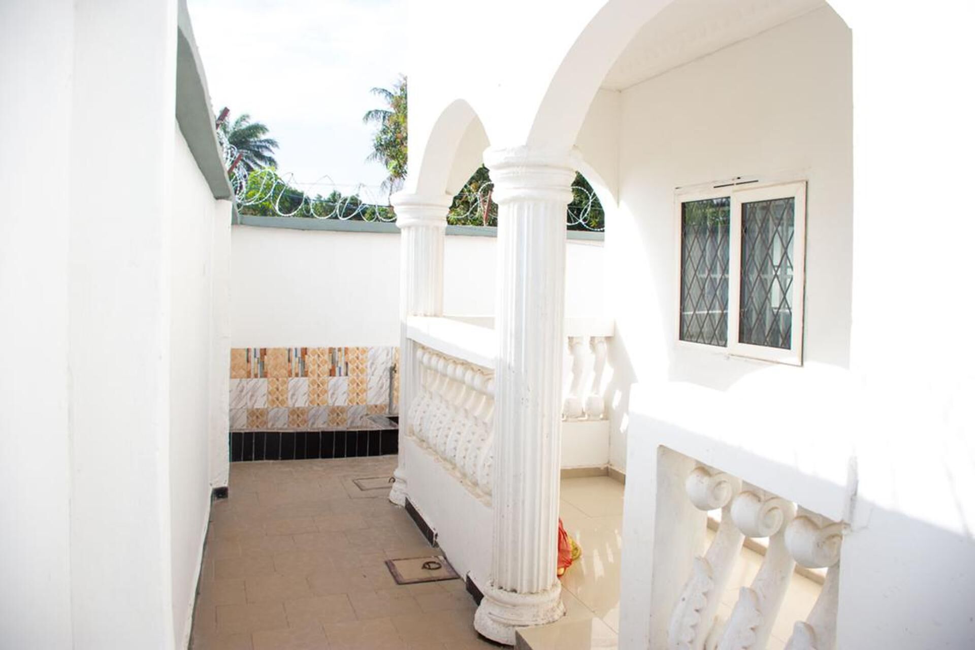 A white corridor with a tiled floor, a window with bars, and a balcony with white railings.