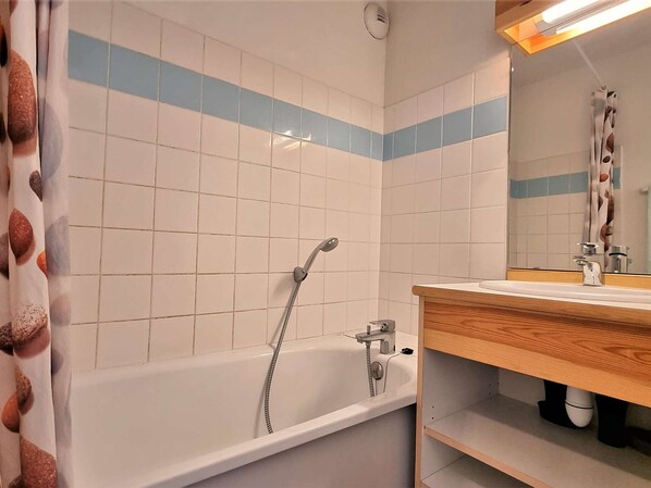 Une salle de bain avec une baignoire, une douche et un meuble-lavabo en bois doté d’un miroir.