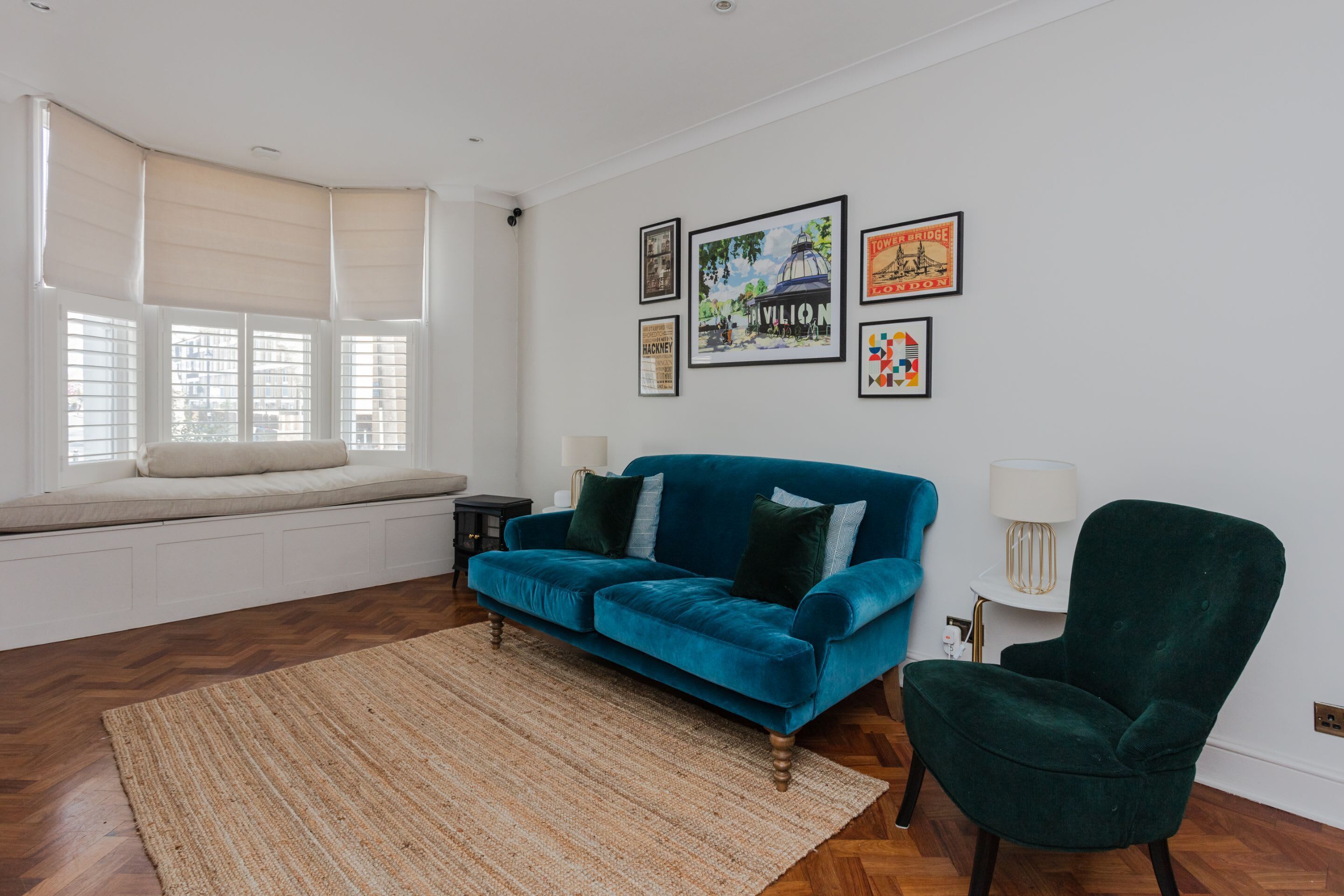 A living room with a blue sofa, a green armchair, a rug, and a bay window with blinds.
