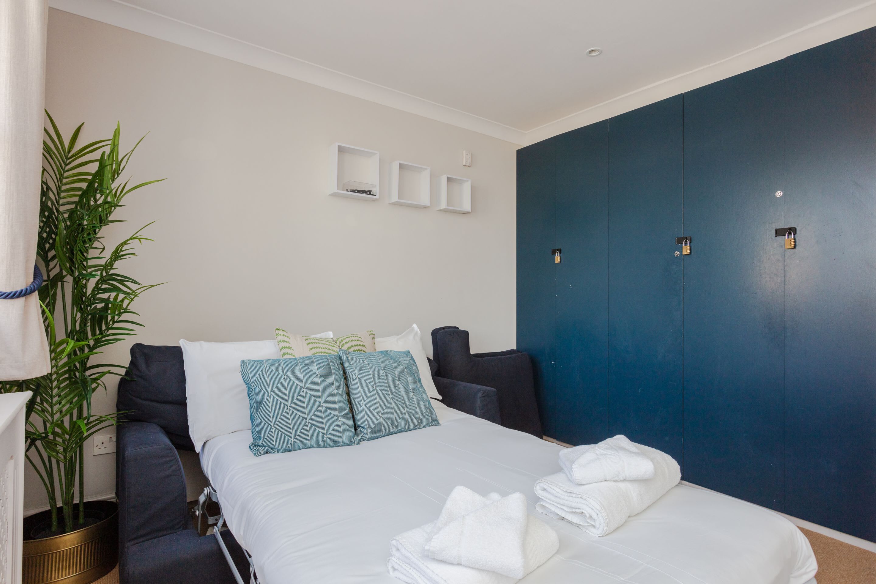 Une chambre d’hôtel avec un lit, une plante en pot et une armoire bleu foncé.