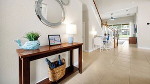 A hallway with a wooden console table, a large mirror, a potted plant, and a wicker basket. - Windsor Hills! Free Pool Heat/BBQ/Waterpark. Game Room w/Theater, Themed Rooms. (Kissimmee)