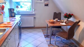 A compact kitchen with a window, a dining table with chairs, and a radiator. - Vacation apartment in a quiet location for 2 people (non-smoking property) (Born)