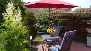 An outdoor patio with a table and chairs, a red umbrella, and a wooden fence in the background. - Vacation apartment in a quiet location for 2 people (non-smoking property) (Born)