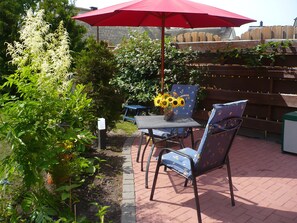 An outdoor patio with a table and chairs, a red umbrella, and a wooden fence in the background. - Vacation apartment in a quiet location for 2 people (non-smoking property) (Born)