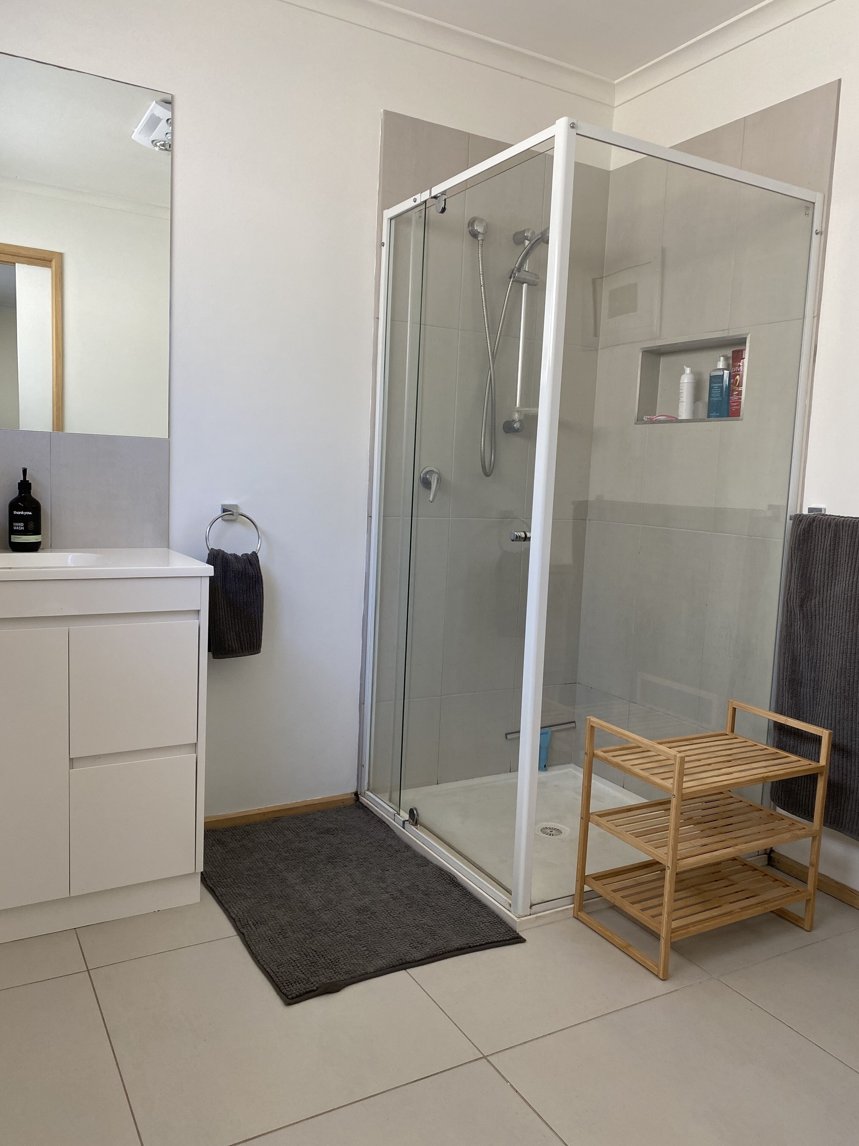 A modern bathroom with a glass-enclosed shower, a white vanity, and a wooden shelf unit.