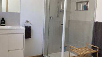 A modern bathroom with a glass-enclosed shower, a white vanity, and a wooden shelf unit.