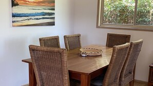 Ein Essbereich mit Holztisch und Korbstühlen, einem gewebten Korb auf dem Tisch und einem Sonnenuntergangsbild an der Wand.