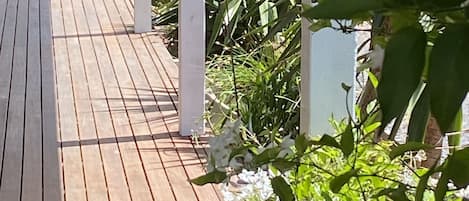 A wooden deck with white pillars, surrounded by greenery and white flowers.
