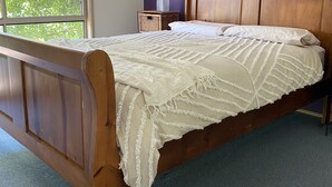 Une chambre avec un lit en bois, un mur violet et une fenêtre donnant sur un paysage verdoyant.