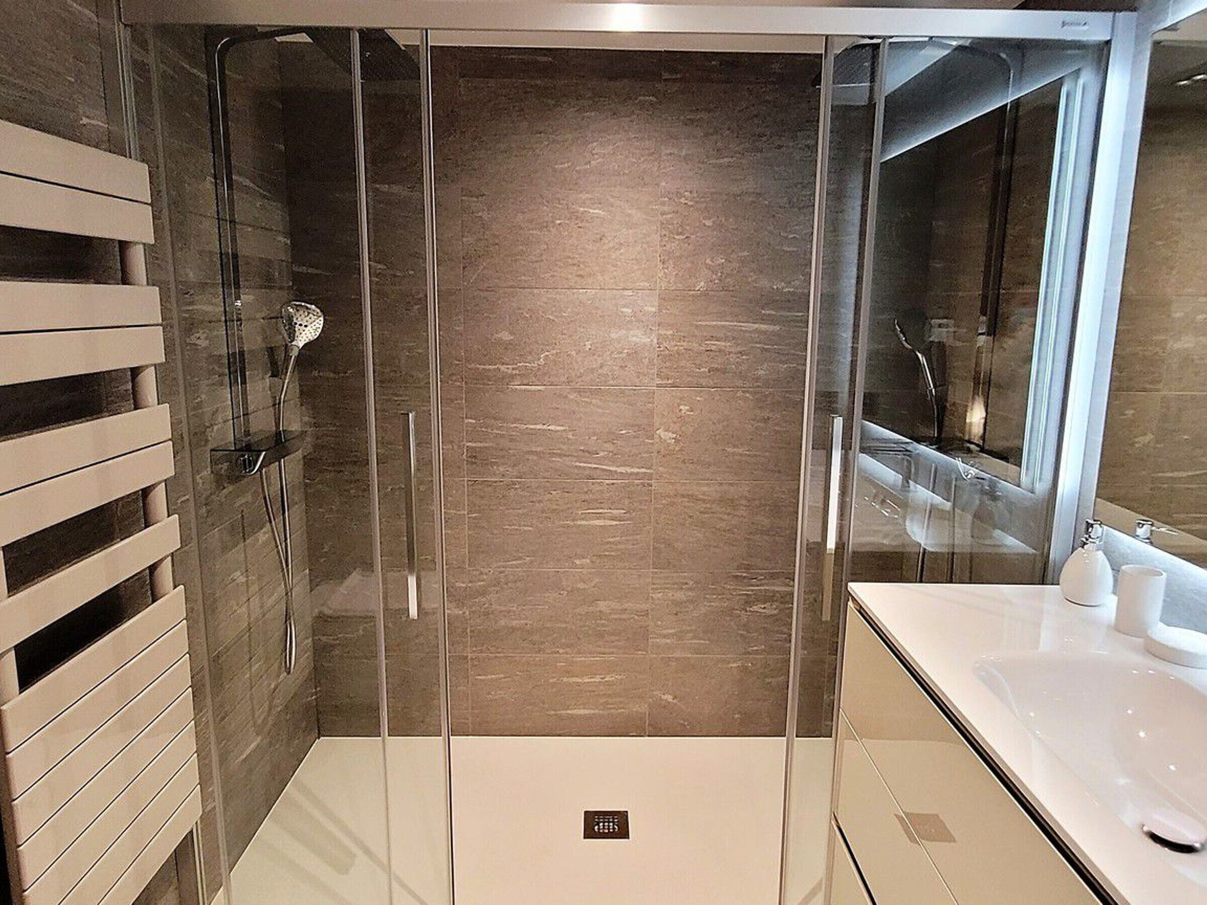 A modern bathroom with a glass-enclosed shower, a white sink, and a large mirror.