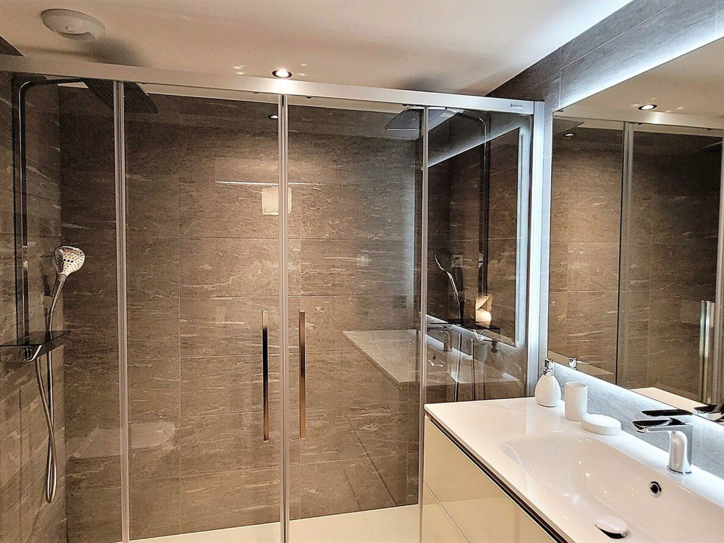 A modern bathroom with a glass-enclosed shower, a large mirror, and a white sink.