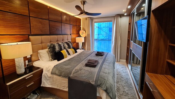 Ein modernes Schlafzimmer mit einem großen Bett, einem Holz-Kopfteil, einer Nachttischlampe und einem Deckenventilator.