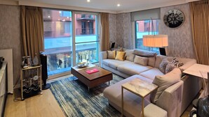 Ein modernes Wohnzimmer mit einer Couch, einem Couchtisch und Blick auf ein Gebäude durch große Fenster.