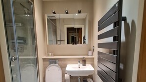 Ein modernes Badezimmer mit Duschkabine aus Glas, Toilette, Waschbecken und Handtuchhalter.
