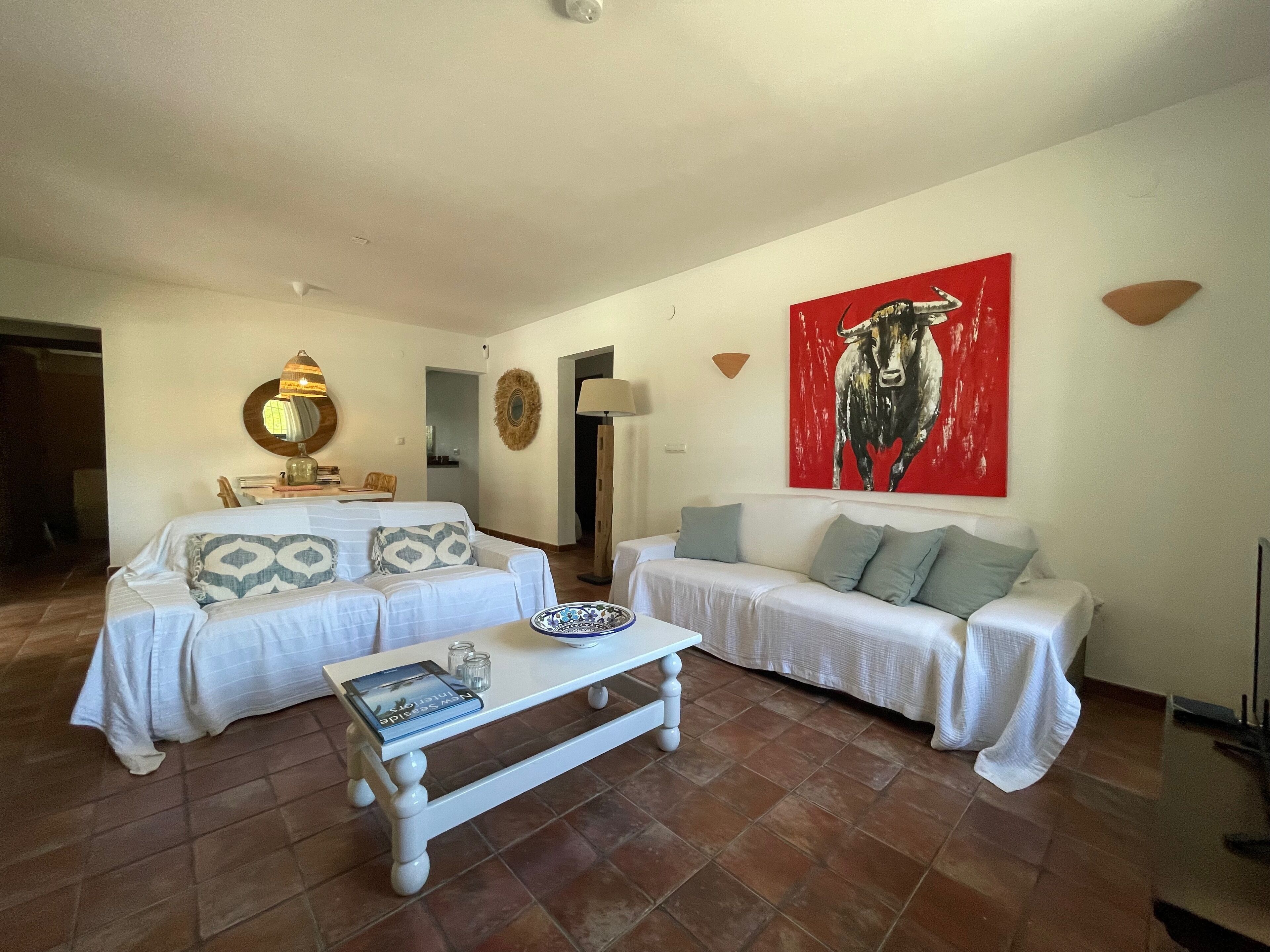 A living room with two white sofas, a coffee table, and a red bull painting on the wall.