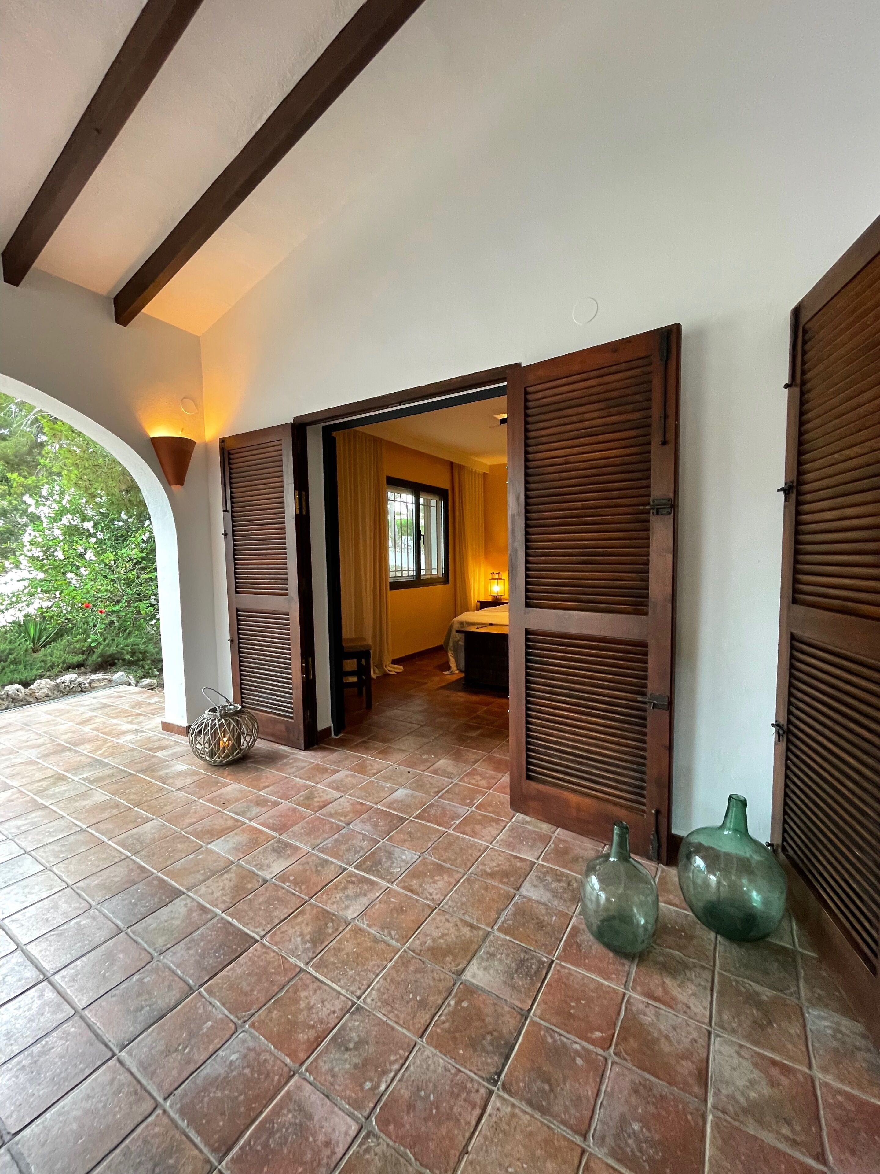 A covered patio with tiled flooring, wooden shutters, and a lantern.