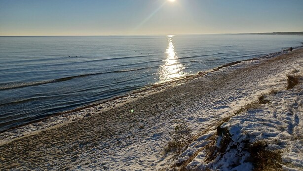 A beach with a clear sky and the sun reflecting on the water.