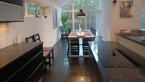 A modern kitchen with a dining area, large windows, and a view of trees.