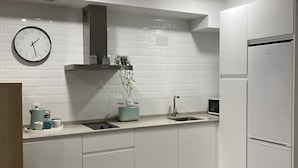 Uma cozinha moderna com armários brancos, forno embutido, pia de aço inoxidável e um relógio na parede.