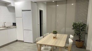 Uma cozinha moderna com armários brancos, geladeira embutida e uma área de jantar com mesa e cadeiras de madeira.