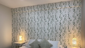 Uma cama bem arrumada com lençóis brancos e duas almofadas, com duas mesinhas de cabeceira e luminárias, em um quarto com papel de parede floral.