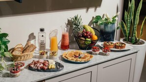 Un bufé de desayuno con diversos alimentos, bebidas y un bol de frutas en una encimera de cocina.
