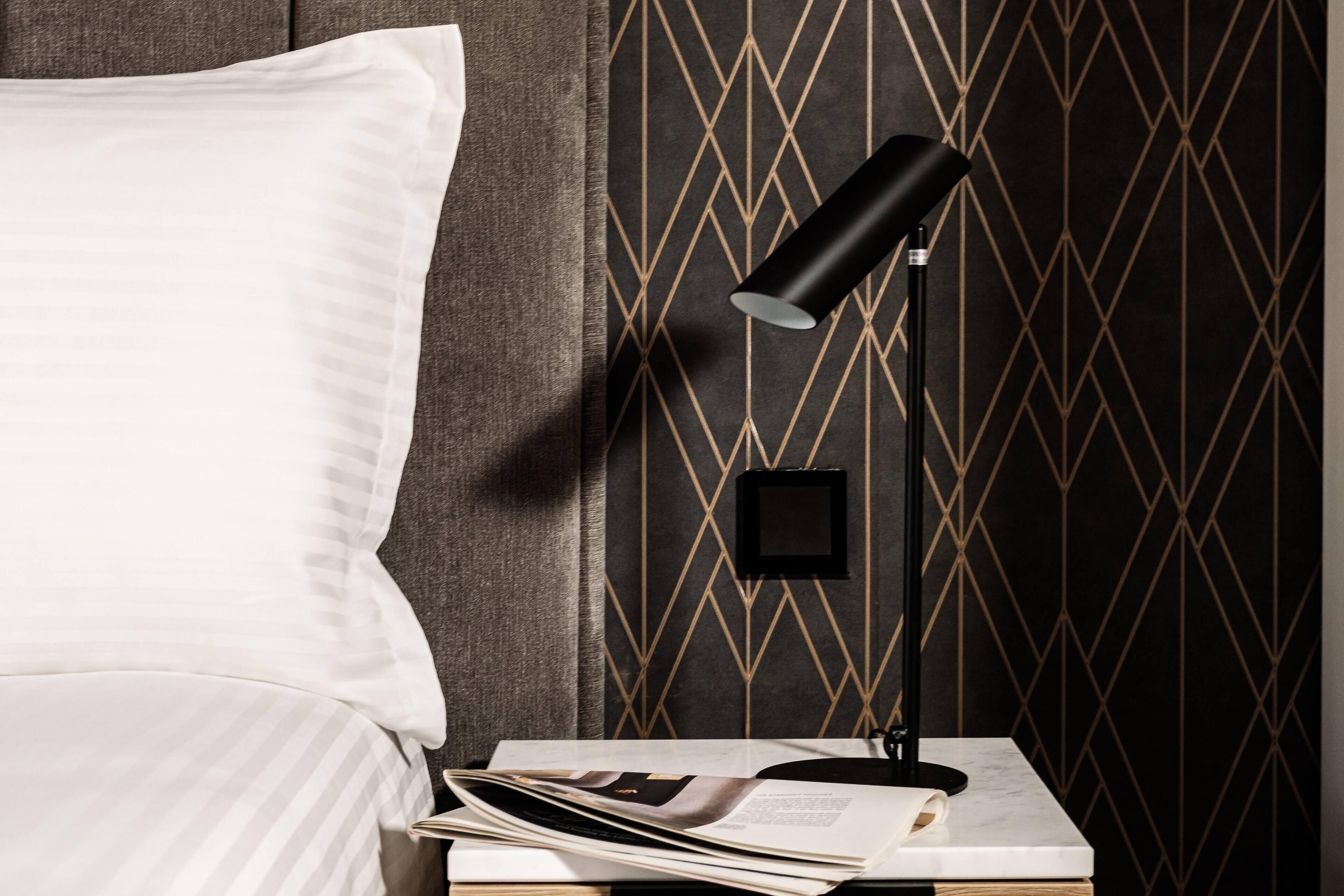A neatly made bed with a white pillow and a black lamp on a bedside table.