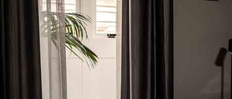 Quarto de hotel com cama, porta com cortinas, uma planta e um quadro na parede.