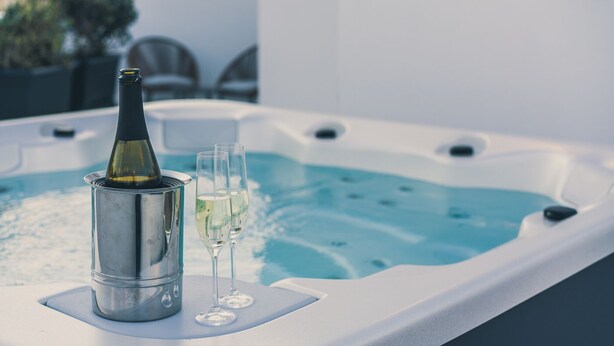 Un jacuzzi con una botella de champán y dos copas sobre una superficie blanca.