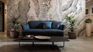 Una sala de estar moderna con una gran pared de mármol, un sofá azul oscuro, dos plantas en macetas y una mesa de centro negra.